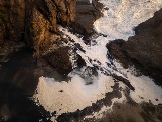 Ocean waves and seafoam crashing over rocks at Piha at sunset, Auckland, New Zealand.