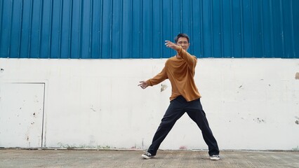 Hispanic man stretch arms and dance street dancing in front of wall. Motion shot of stylish dancer...