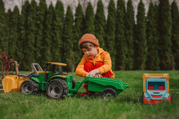 Boy crouching and playing with toy tractor on green grass in back yard