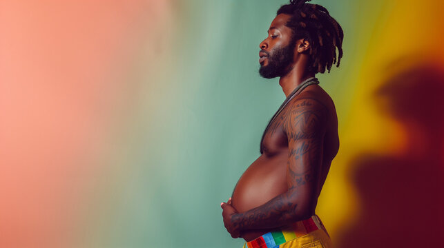 Profile shot of tattooed afro-caribbean black pregnant man at pride celebration shoot with pastel coloured studio background