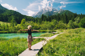 People in nature. Tourist woman with raised arms up in green nature background. View on Zelenci (into English means - green) natural reserve in Slovenia, Europe. Travel, Freedom, Lifestyle concept.