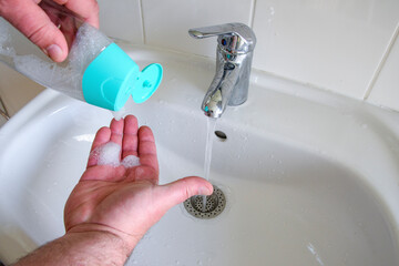 Ran out of soap in the bathroom. A man is washing his hands in a sink with a bottle of soap in his...