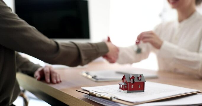 Real estate agent gives key to new cottage house to female customer. Women shake hands after making successful deal in office slow motion
