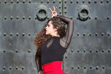 Obraz premium Portrait of young, beautiful, brunette woman in black shirt and red skirt, dancing flamenco with old, black metal door in the background. Flamenco concept, dance, art, typical Spanish.