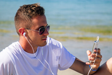 young man listening to music with his headphones and mobile phone on the beach