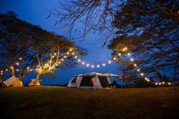 camping tent on grass courtyard and warm night light under dark blue sky. Family vacation picnic on...