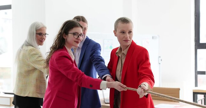 Purposeful colleagues man and women in formal suits pull rope and have fun at break in company office. Delighted collective develops teamwork slow motion
