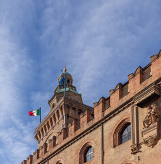 Fototapeta na wymiar The Italian flag flutters proudly atop Palazzo d'Accursio in Bologna, its historical facade a testament to the city rich past, against a blue sky