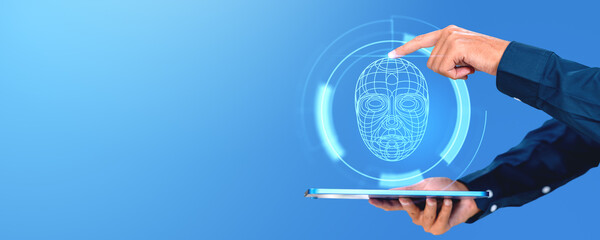 A person interacting with a holographic face recognition interface on a tablet, set against a blue...