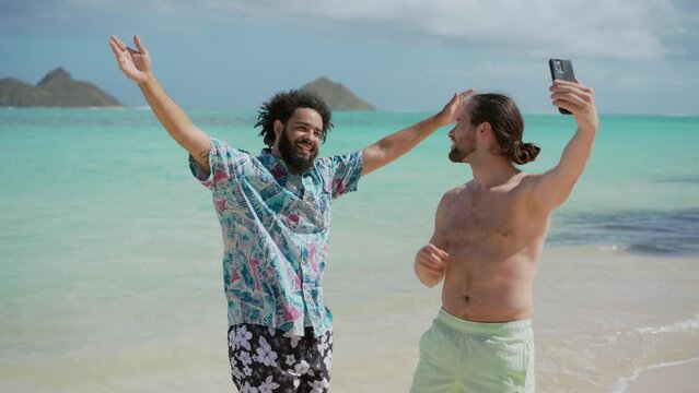 Two euphoric men celebrate their beach day with a selfie, arms raised in joy against a backdrop of the stunning turquoise ocean, embodying the spirit of a perfect vacation. Slow motion. 