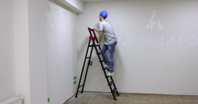 Male builder climbs to top of construction ladder in light premise. Preparing flat for renovation. Checking condition of apartment walls slow motion