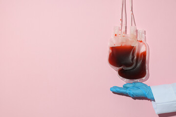 Bags with donor blood and doctor's hand on pink background, space for text