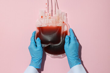 Bags with donor blood in doctor's hands on pink background, top view