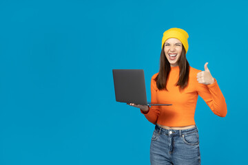 A girl in a yellow hat with a laptop on a blue background.