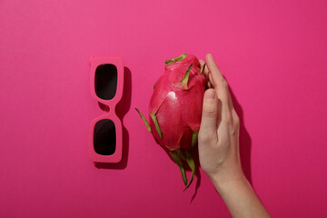 Dragon fruit in hand and sunglasses on pink background, top view