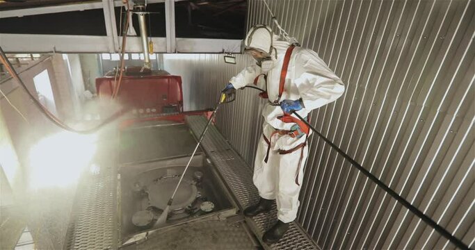 Automatic steam cleaning of the tanker. Worker in chemical protection. A worker makes a chemical cleaning of a tank truck with steam from the inside.