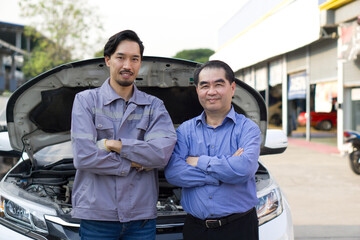A mechanic in work uniform and senior customer, stand with their arm cross, in front of an open car hood at car dealership, satisfaction with a repair or inspecting the vehicle service.