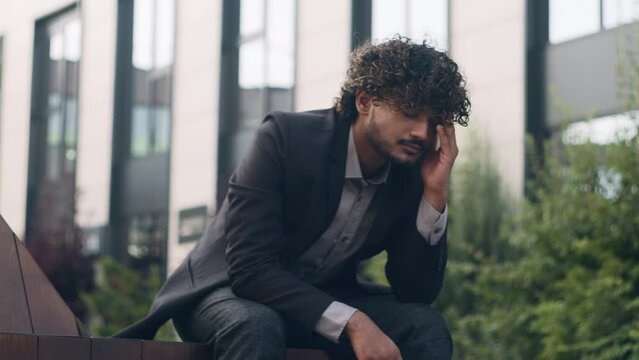 Suffering anxious worried irritated Indian business man feeling bad headache frustrated problem businessman employer manager entrepreneur in city outdoors thinking about corporate trouble headache