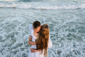 Love. Couple hugging on seashore in sea. Male hugs female standing on water with big waves ocean and enjoying a summer day. Man embraces woman walking on beach sand sea. Top view.