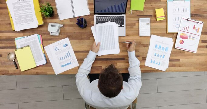 Male employee examines documents with diagrams circling relevant information. Man creates strategy of company development slow motion