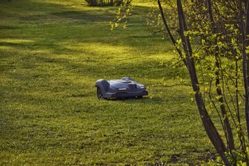 Robotic lawnmower working in the garden with headlights on in the evening