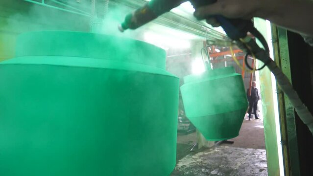 Worker spraying green paint on detail in painting chamber. Painter working at industrial manufacture. Master paint detail in specialised workshop. Man painting parts in production. Slow motion Closeup