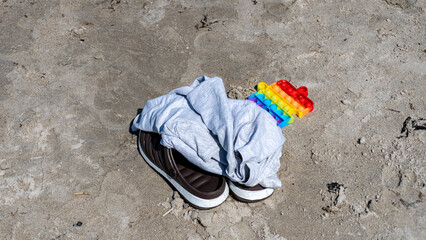 shirt, shoes and toy left on the sandy beach on summer holidays