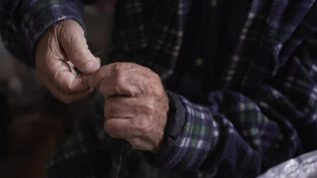 detail of an old man's hands tightening aluminium wire and spinning it in the workshop, manual restoration work by old, weathered hands.