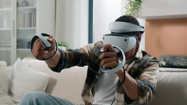 African American man player enjoying cyberspace metaverse meta world at home playing vr game ethnic guy gamer male play online wearing virtual reality 3d helmet glasses hold controllers joysticks