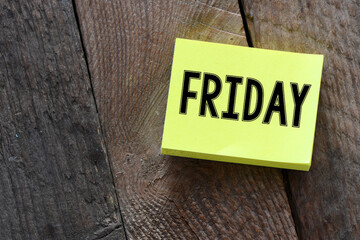 The word FRIDAY on a small piece of paper laid on a wooden table.