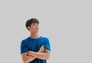 A young Asian man in his 20s wearing a blue t-shirt standing with arms crossed and showing a sad or sad expression isolated on gray background. stress concept