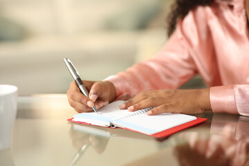 Black woman hands writing in paper agenda at home