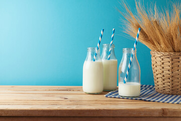 Jewish holiday Shavuot concept with milk bottles and wheat ears in basket on wooden table over blue...