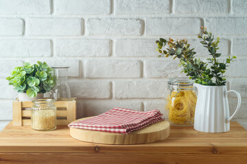 Empty wooden log  and tablecloth on kitchen table with food jars and plants over white brick wall ...