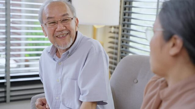 Asian grandfather talking with grandmother sitting on couch in the living room. Senior couple enjoy weekend together at home.