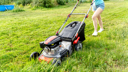 A girl with a lawnmower mows the lawn in the garden