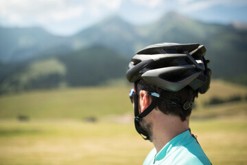 Rear view of cyclist in helmet admire mountains and beautiful nature, standing by bicycle. Concept of healthy lifestyle.