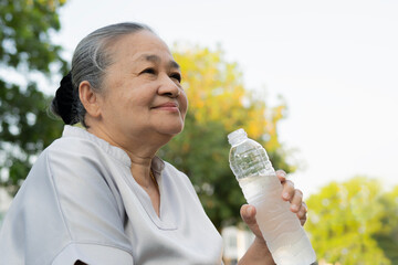 Smiling active senior woman holding water bottles, drink while relaxing in the park.