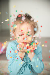 Obraz na płótnie Canvas A sweet girl holds confetti in her hands and blows it away. She wears a bright smile as she enjoys the playful moment, creating an atmosphere of joy and excitement. The colorful confetti flies through