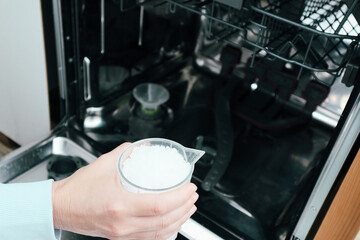 A woman pours industrial salt into the dishwasher. A woman adds salt to the detergent solution in the dishwasher.