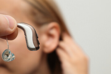 Deaf patient with audiology implant. Close up of woman hand holding digital hearing aid. Unrecognizable woman putting on a modern hearing aid on her ear. Stylish hearing device