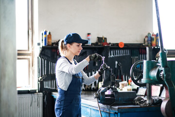Female auto mechanic repairing, maintaining car. Beautiful woman working in a garage, wearing blue...
