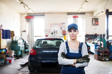 Female auto mechanic repairing, maintaining car. Beautiful woman standing in a garage, wearing blue...