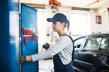 Female auto mechanic repairing, maintaining car. Beautiful woman working in a garage, wearing blue...