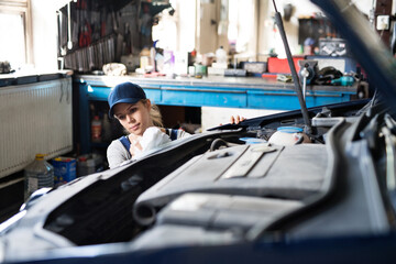 Female auto mechanic repairing, maintaining car. Beautiful woman working in a garage, wearing blue...