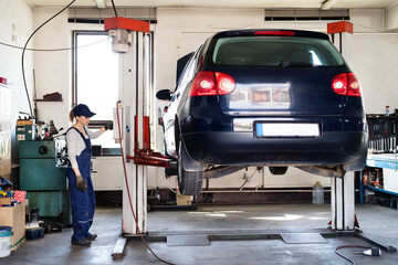 Female auto mechanic elevating car on car lift, working underneath. Beautiful woman working in a...