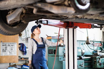 Female auto mechanic elevating car on car lift, working underneath. Beautiful woman working in a...