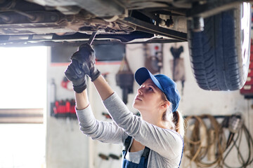 Female auto mechanic elevating car on car lift, working underneath. Beautiful woman working in a...