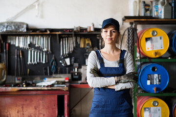 Female auto mechanic repairing, maintaining car. Beautiful woman standing in a garage, wearing blue coveralls.