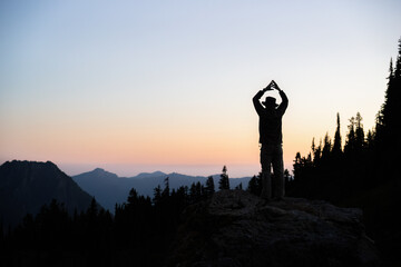 Man standing on rocks with arms raised. Paradise at sunset. Mount Rainier National Park. Washington...